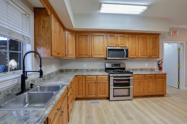504 E Church St, Champaign, IL 61820 - kitchen featuring appliances with stainless steel finishes, a sink, light wood finished floors, and brown cabinetry