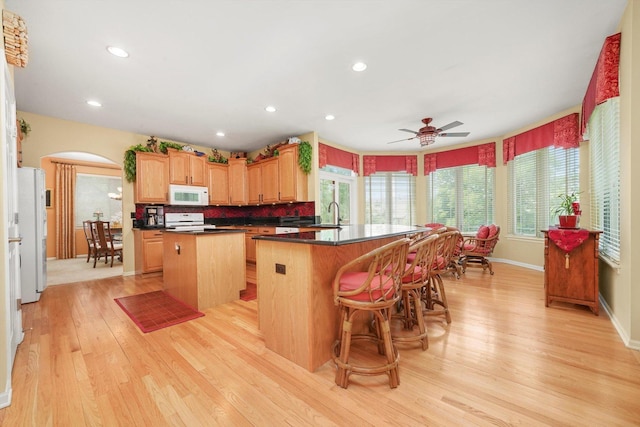 25014 W Nicklaus Way, Antioch, IL 60002 - kitchen featuring white appliances, a kitchen island, arched walkways, light wood-style flooring, and healthy amount of natural light
