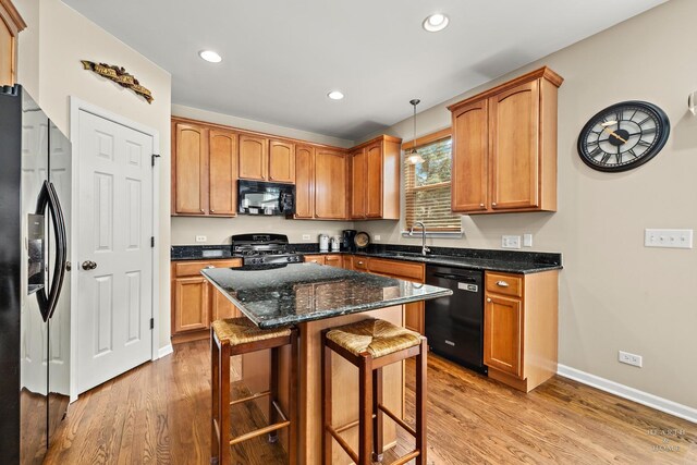 11582 Beacon Ave, Huntley, IL 60142 - kitchen with black appliances, a sink, light wood-style floors, a breakfast bar area, and dark stone countertops