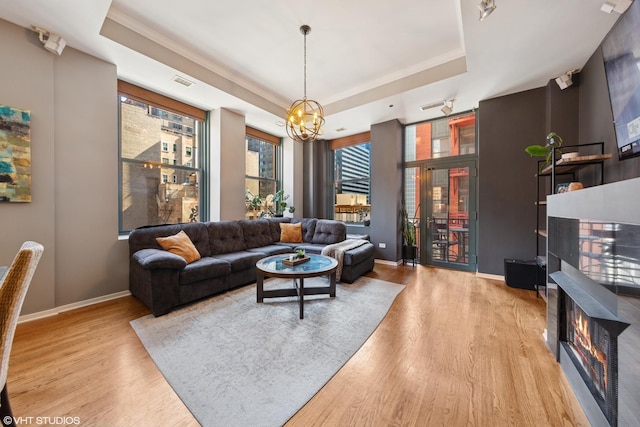 208 W Washington St Unit 1205, Chicago, IL 60606 - living area featuring wood finished floors, a chandelier, a tray ceiling, a glass covered fireplace, and crown molding