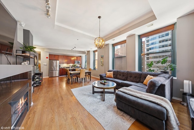 208 W Washington St Unit 1205, Chicago, IL 60606 - living room featuring a tray ceiling, a chandelier, light wood-style flooring, and a glass covered fireplace