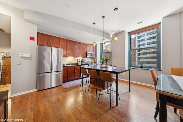 208 W Washington St Unit 1205, Chicago, IL 60606 - kitchen featuring appliances with stainless steel finishes, wood finished floors, decorative light fixtures, decorative backsplash, and a breakfast bar