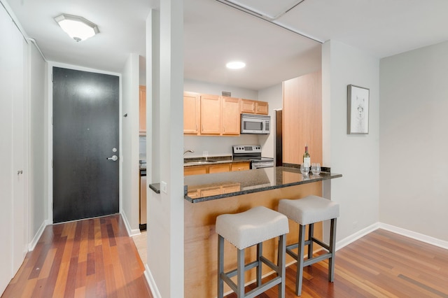 535 N Michigan Ave Unit 2205, Chicago, IL 60611 - kitchen featuring stainless steel appliances, light brown cabinetry, light wood-style flooring, and a kitchen bar