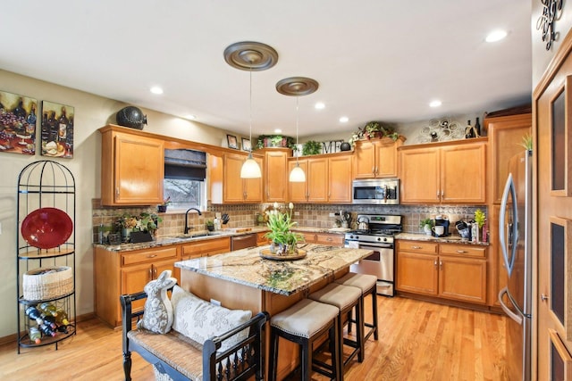 949 Ruthenbeck Ln, New Lenox, IL 60451 - kitchen featuring appliances with stainless steel finishes, light wood-type flooring, decorative backsplash, a kitchen island, and light stone countertops