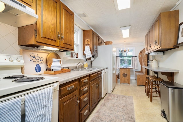 735 W Henry St, Pontiac, IL 61764 - kitchen featuring white appliances, under cabinet range hood, a chandelier, light countertops, and brown cabinetry