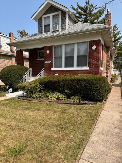bungalow featuring brick siding, a front lawn, and a chimney