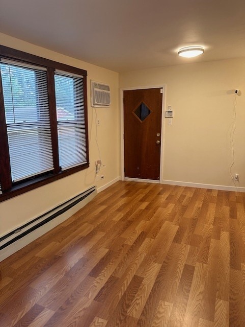 spare room with an AC wall unit, baseboard heating, baseboards, and light wood finished floors