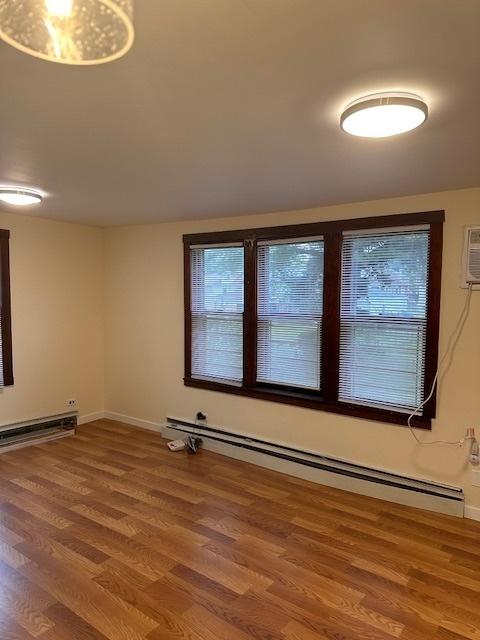 empty room featuring a baseboard heating unit, plenty of natural light, wood finished floors, and baseboards