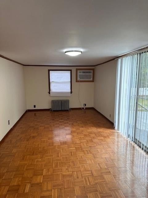spare room featuring radiator heating unit, an AC wall unit, baseboards, and crown molding