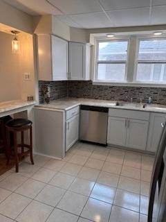 kitchen featuring stainless steel dishwasher, gray cabinetry, backsplash, light countertops, and light tile patterned floors