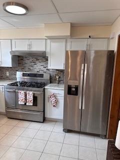 kitchen with stainless steel appliances, light countertops, light tile patterned floors, white cabinetry, and decorative backsplash