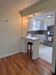 kitchen with stainless steel range oven, tasteful backsplash, a peninsula, light wood-style floors, and a breakfast bar area