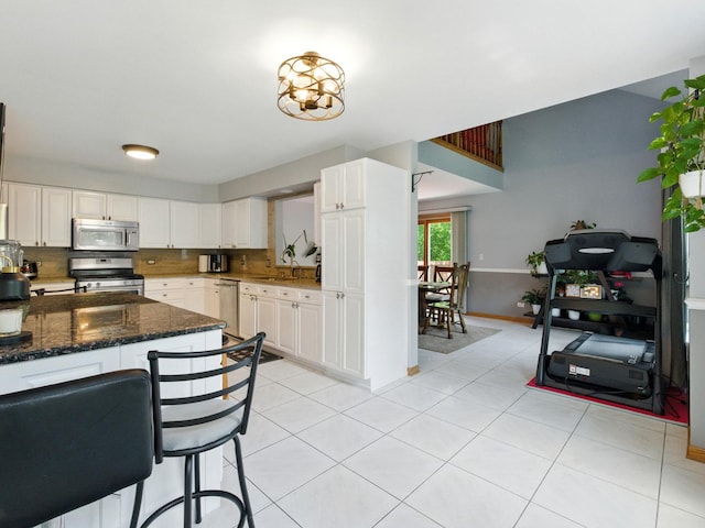 1386 Laurel Oaks Dr, Streamwood, IL 60107 - kitchen featuring appliances with stainless steel finishes, white cabinets, light tile patterned floors, dark stone countertops, and backsplash