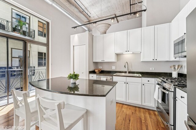 758 N Larrabee St Unit 427, Chicago, IL 60654 - kitchen featuring stainless steel appliances, a sink, light wood finished floors, white cabinets, and a high ceiling