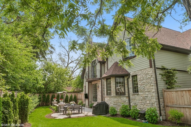 1219 Parkside Ln, Deerfield, IL 60015 - back of property featuring stone siding, a patio, a shingled roof, and a fenced backyard