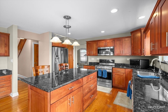 431 Blue Ridge Ct, Oswego, IL 60543 - kitchen with stainless steel appliances, light wood-style flooring, a kitchen island, dark stone countertops, and decorative light fixtures