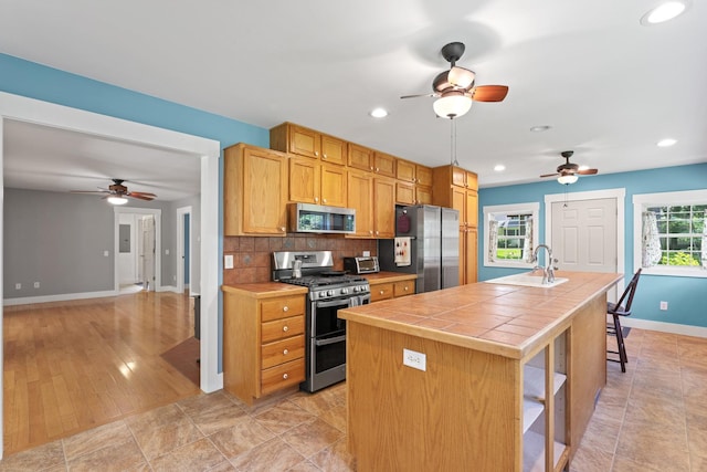 1046 N Riverside Dr, Momence, IL 60954 - kitchen with appliances with stainless steel finishes, tile countertops, ceiling fan, decorative backsplash, and a kitchen island with sink