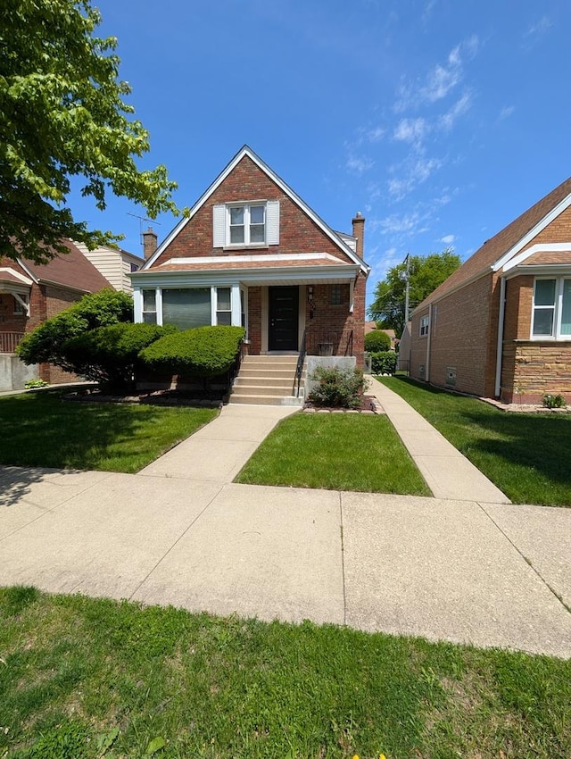 bungalow with brick siding, a front yard, a chimney, and covered porch