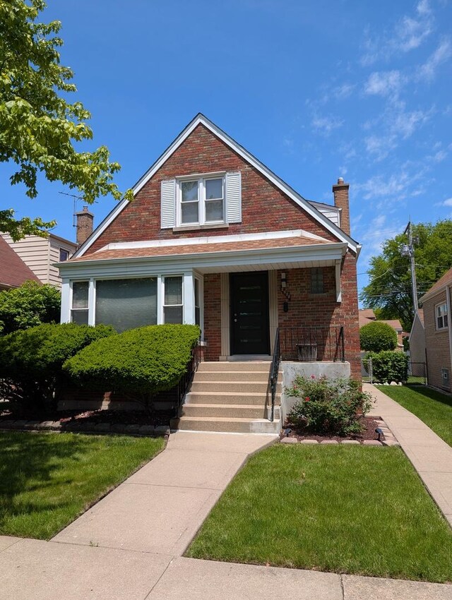 bungalow featuring brick siding, a porch, a chimney, and a front yard