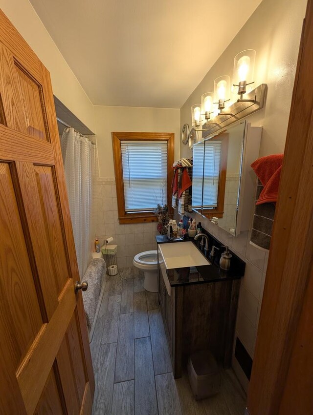 full bathroom featuring tile walls, wood finished floors, vanity, shower / bath combo with shower curtain, and wainscoting