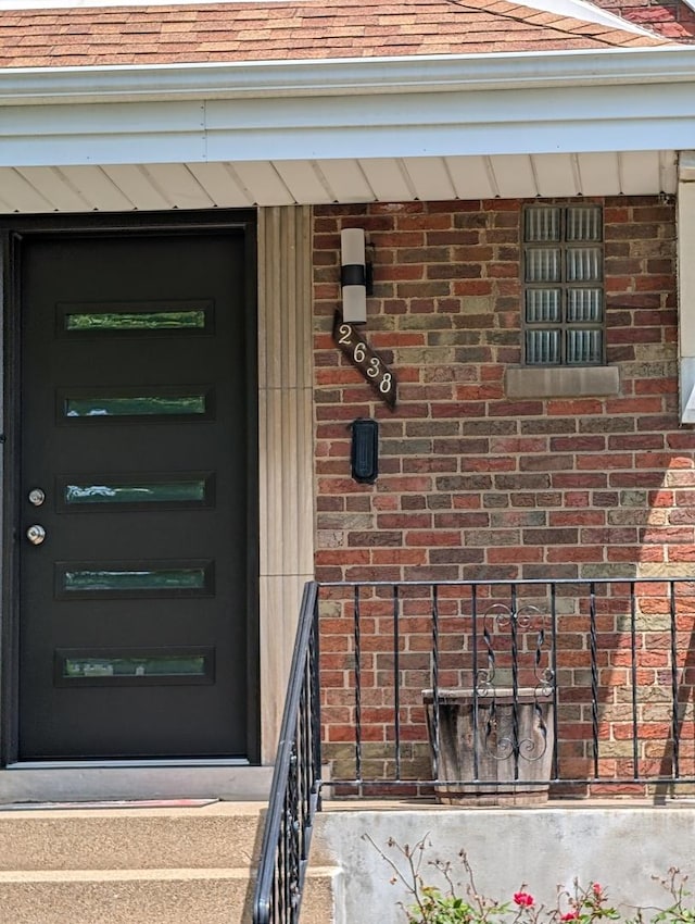 entrance to property with brick siding and a shingled roof