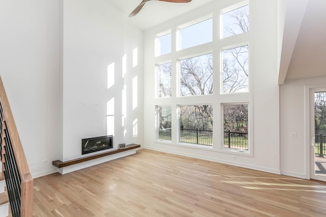 26205 Stewart Ridge Dr, Plainfield, IL 60585 - unfurnished living room featuring a high ceiling, light wood-style floors, a glass covered fireplace, and a ceiling fan