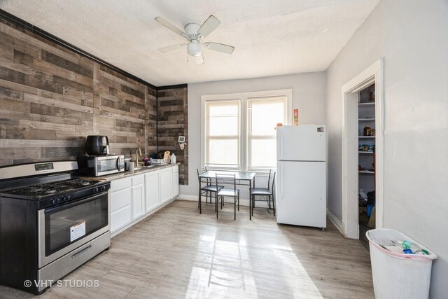 7514 S Dante Ave, Chicago, IL 60619 - kitchen featuring stainless steel appliances, a ceiling fan, wood walls, white cabinetry, and light wood-style flooring