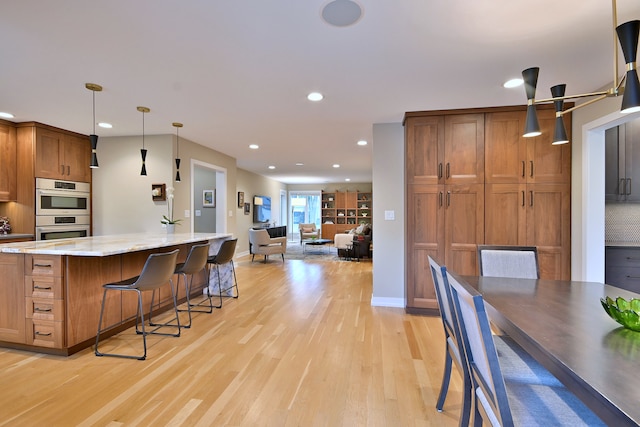 717 S Washington St, Elmhurst, IL 60126 - kitchen with double oven, light wood-style flooring, brown cabinets, light stone countertops, and a breakfast bar