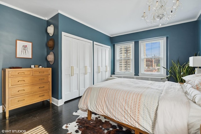 bedroom featuring two closets, dark wood-type flooring, a chandelier, and ornamental molding