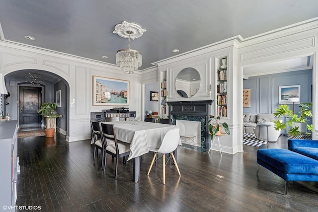 dining room with arched walkways, a chandelier, ornamental molding, hardwood / wood-style flooring, and a fireplace