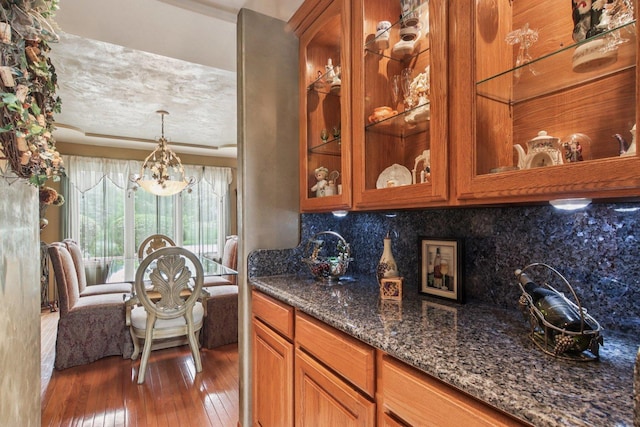 22454 Hinspeter Dr, Frankfort, IL 60423 - kitchen with brown cabinetry, hardwood / wood-style flooring, a chandelier, dark stone counters, and decorative backsplash