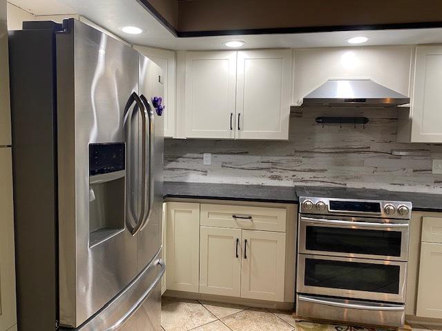 23 Acapulco Dr, Putnam, IL 61560 - kitchen with appliances with stainless steel finishes, ventilation hood, decorative backsplash, light tile patterned flooring, and dark countertops