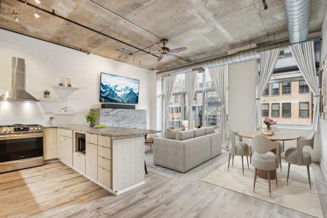 1000 W Adams St Unit 523, Chicago, IL 60607 - kitchen with stainless steel range with gas stovetop, wall chimney range hood, light wood finished floors, a ceiling fan, and light brown cabinetry