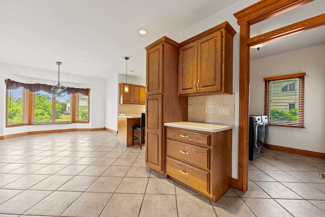552 Waters Edge Dr, South Elgin, IL 60177 - kitchen with washing machine and clothes dryer, brown cabinetry, light countertops, backsplash, and light tile patterned floors