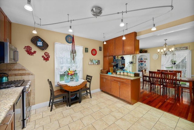 233 S Elmwood Dr, Aurora, IL 60506 - kitchen with stainless steel appliances, brown cabinetry, a chandelier, light stone countertops, and decorative light fixtures