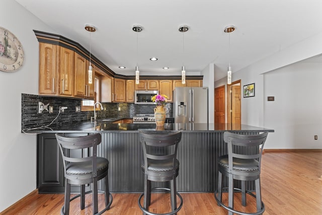 925 Magnolia Dr, Bourbonnais, IL 60914 - kitchen featuring appliances with stainless steel finishes, a peninsula, decorative backsplash, a breakfast bar area, and light wood finished floors