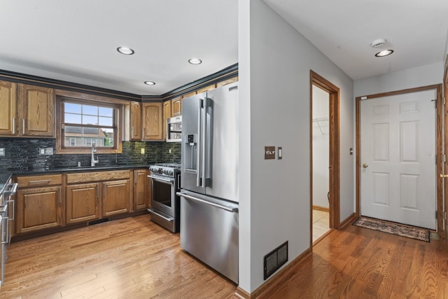 925 Magnolia Dr, Bourbonnais, IL 60914 - kitchen featuring appliances with stainless steel finishes, light wood finished floors, brown cabinetry, tasteful backsplash, and recessed lighting