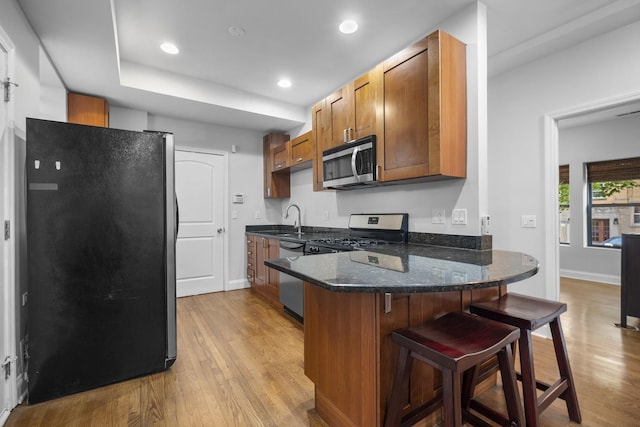 3316 W Byron St Unit 1, Chicago, IL 60618 - kitchen featuring appliances with stainless steel finishes, brown cabinetry, light wood-style flooring, a peninsula, and a breakfast bar area