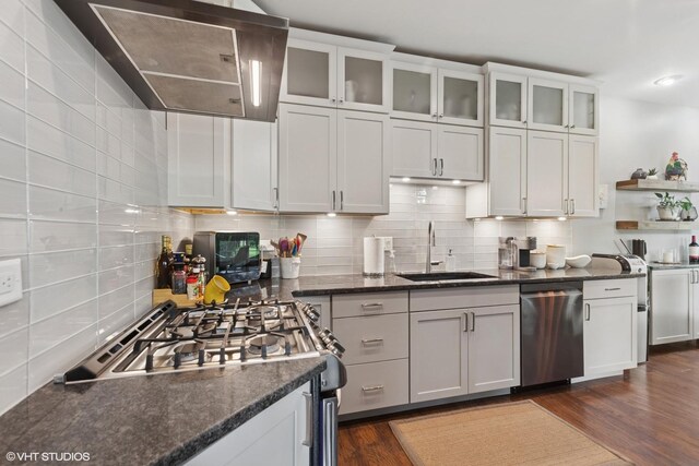 kitchen with stainless steel appliances, wall chimney range hood, decorative backsplash, white cabinets, and glass insert cabinets