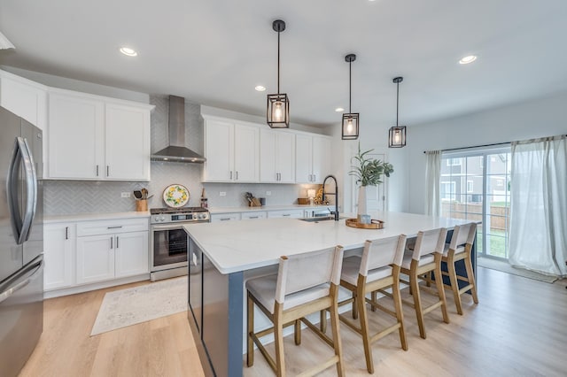 25320 W Alison Rd, Plainfield, IL 60586 - kitchen featuring wall chimney exhaust hood, stainless steel appliances, light wood-style floors, decorative backsplash, and a center island with sink