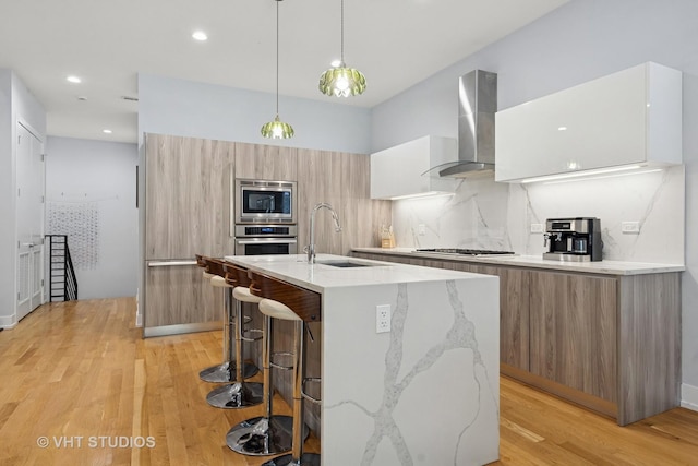 5236 N Kenmore Ave Unit 1N, Chicago, IL 60640 - kitchen featuring modern cabinets, wall chimney range hood, stainless steel appliances, light wood-style flooring, and a center island with sink