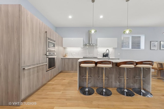 5236 N Kenmore Ave Unit 1N, Chicago, IL 60640 - kitchen featuring modern cabinets, wall chimney range hood, stainless steel appliances, a breakfast bar, and light wood-type flooring