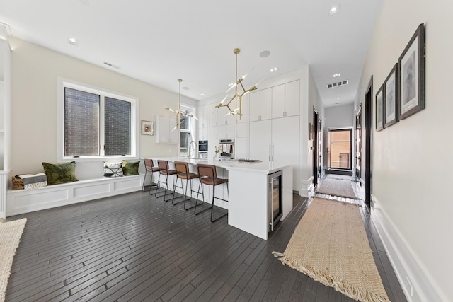 2756 N Magnolia Ave Unit Ph, Chicago, IL 60614 - kitchen with a breakfast bar area, white cabinetry, dark wood finished floors, light countertops, and decorative light fixtures