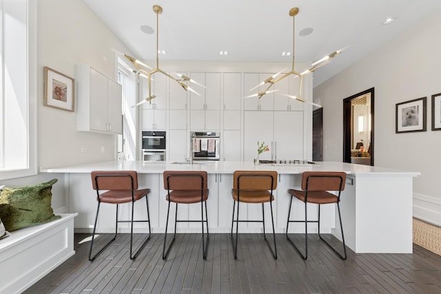 2756 N Magnolia Ave Unit Ph, Chicago, IL 60614 - kitchen featuring dark wood finished floors, white cabinets, a kitchen breakfast bar, a peninsula, and light countertops