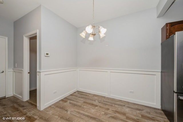 2733 Kendall Xing, Johnsburg, IL 60051 - unfurnished dining area featuring a chandelier, wood finished floors, a wainscoted wall, and a decorative wall