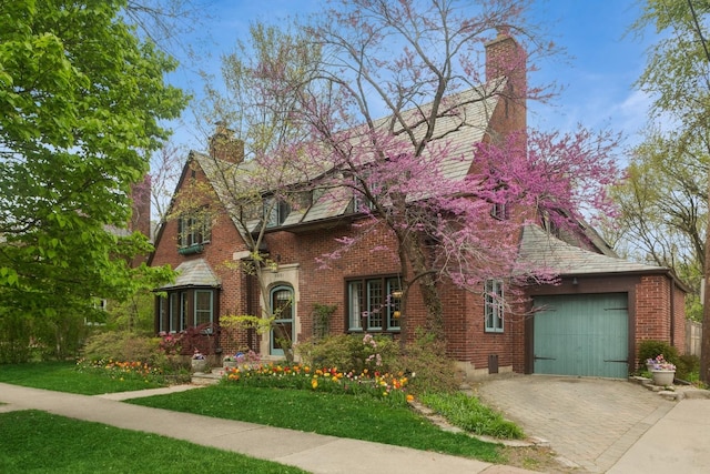 2951 Colfax St, Evanston, IL 60201 - tudor home with a chimney, decorative driveway, brick siding, an attached garage, and a front yard