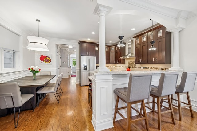 1430 W Diversey Pkwy Unit 1, Chicago, IL 60614 - kitchen featuring ornate columns, stainless steel refrigerator with ice dispenser, wall chimney exhaust hood, crown molding, and dark brown cabinetry