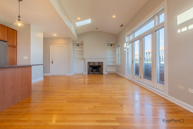 3454 N Ashland Ave Unit 4S, Chicago, IL 60657 - unfurnished living room featuring light wood-style floors, a premium fireplace, a skylight, vaulted ceiling, and built in shelves
