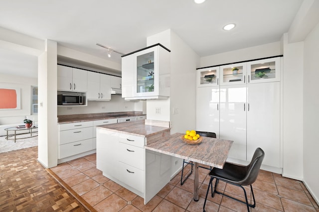 3180 N Lake Shore Dr Unit 8A, Chicago, IL 60657 - kitchen with stainless steel microwave, a kitchen breakfast bar, cooktop, glass insert cabinets, and white cabinetry