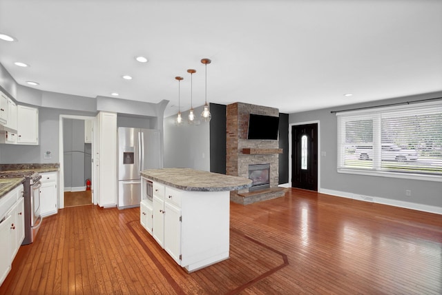 717 Bittersweet Ln, New Lenox, IL 60451 - kitchen featuring appliances with stainless steel finishes, a kitchen island, a fireplace, hardwood / wood-style floors, and white cabinets